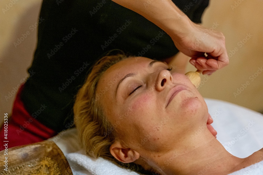 Masseuse giving a facial massage to a client with wood therapy Masseuse giving a facial massage to a client with wood therapy
