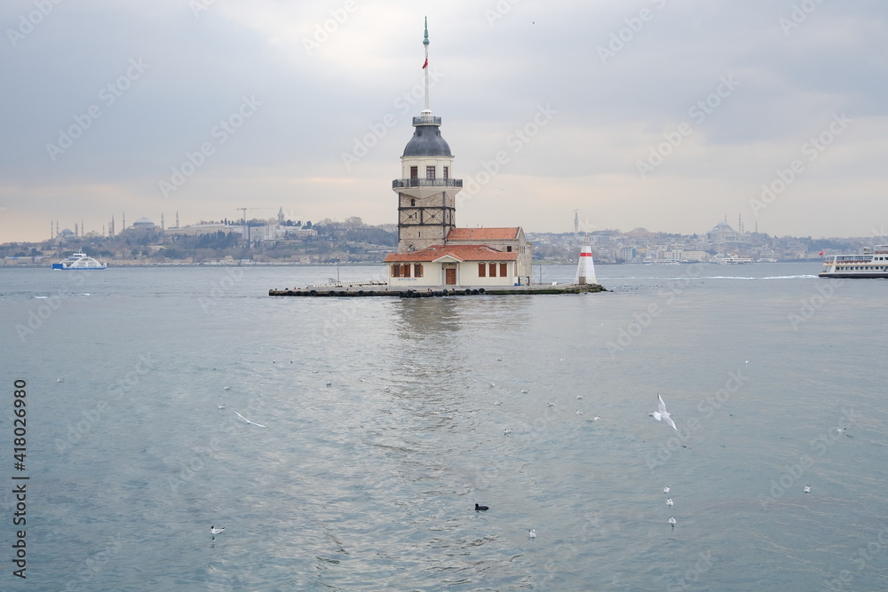 The maiden's tower (kız kulesi) in İstanbul, Turkey during overcast weather with sunshine reflection in bosporus sea.  Groups of seagulls flying on sea. İstanbul Turkey 01.03.2021
