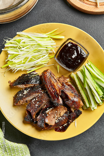 Peking duck chinese food. Yellow plate with vegetables and sauce on dark slate table. Chinese, asian, authentic food concept photo