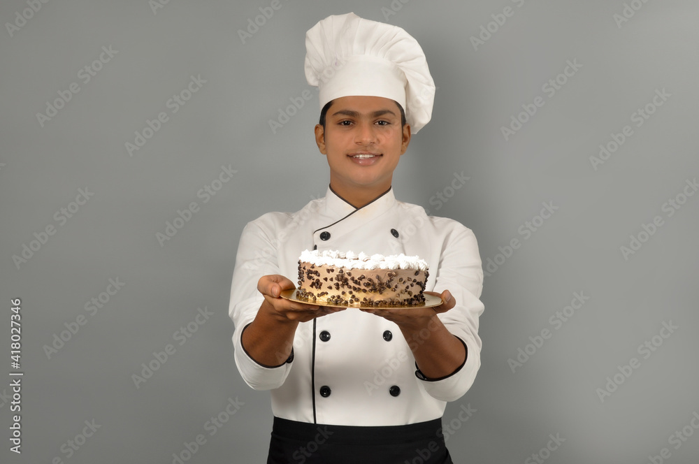 Portrait of a happy male chef dressed in uniform holding plate with Chocolate cake Portrait of a happy male chef dressed in uniform holding plate with Chocolate cake