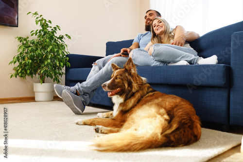Young loving couple relaxing in living room with their dog pet
