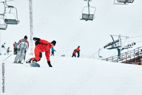 Male snowboarder in a red suit rides on the snowy hill with snowboard, Skiing and snowboarding concept