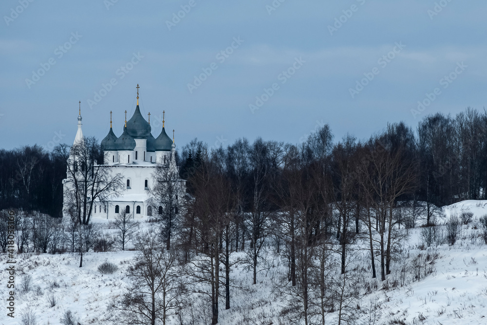 The old stone temple of the city of Tutaev on the bank of the Volga River. Holy Cross Cathedral is an example of local architecture of the mid-XVII century. White temple with blue domes in winter on a