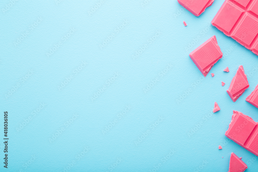 Broken pink chocolate pieces on light blue table background. Pastel color. Sweet snack. Closeup. Empty place for text. Top down view. Broken pink chocolate pieces on light blue table background. Pastel color. Sweet snack. Closeup. Empty place for text. Top down view.