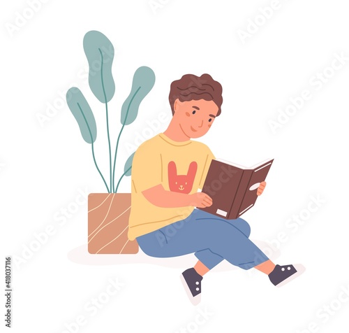 Happy boy sitting with open book in hands and reading it. Smiling kid studyin...