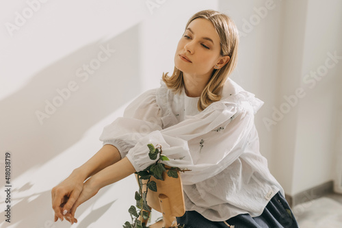 Photographie Young blonde woman sitting on a chair, wearing a white blouse.