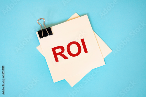 Text ROI on sticky notes with copy space and paper clip isolated on red background.Finance and economics concept.