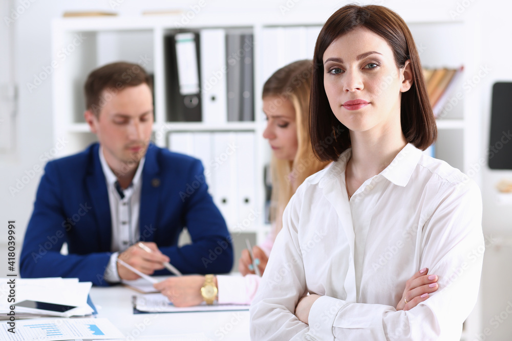 Beautiful girl at workplace look in camera with colleagues group in background hands crossed. White collar worker at workspace, job offer, modern lifestyle, client visit, profession train concept Beautiful girl at workplace look in camera with colleagues group in background hands crossed. White collar worker at workspace, job offer, modern lifestyle, client visit, profession train concept