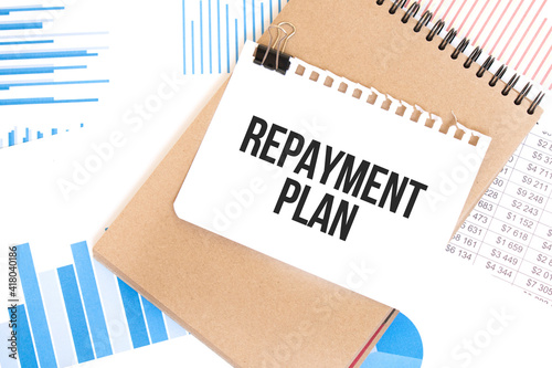 Text repayment plan on white paper sheet and brown paper notepad on the table with diagram. Business concept photo