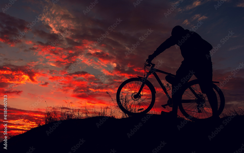 Obraz premium cyclist with a bicycle, in the background fiery sunset.