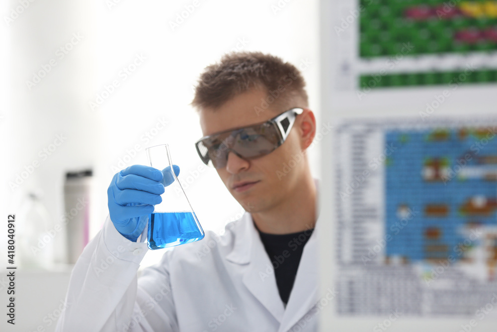 A male chemist holds test tube of glass in his hand overflows a liquid solution of potassium permanganate conducts an analysis reaction takes various versions of reagents using chemical manufacturing A male chemist holds test tube of glass in his hand overflows a liquid solution of potassium permanganate conducts an analysis reaction takes various versions of reagents using chemical manufacturing