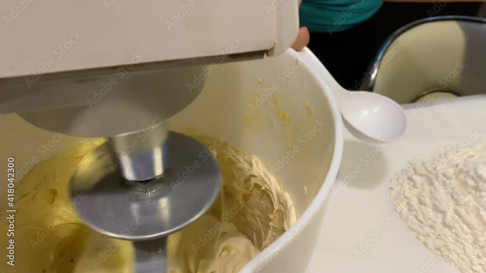scooping spoonfuls of flour into big bowl of cake batter on stand mixer - close up