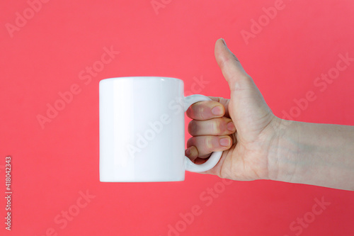 Woman holding a white mug in hand against coral color background