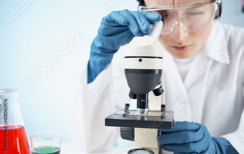 woman in a medical gown in blue gloves stands near the flask and biology chemical element vaccination