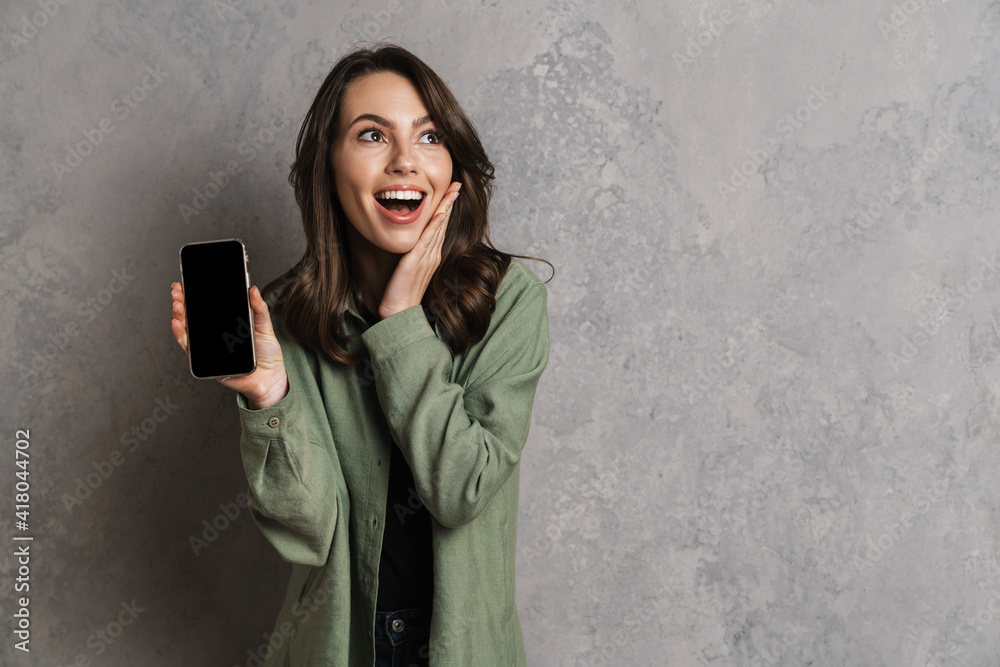 Fototapeta premium Excited caucasian girl looking aside while showing cellphone