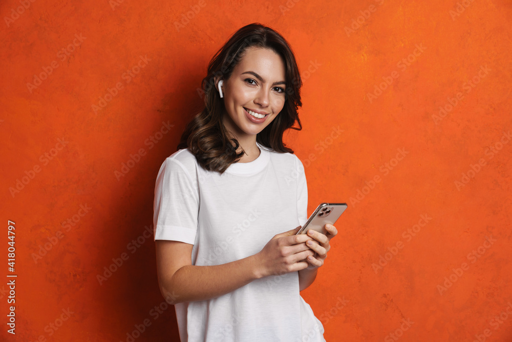 Happy girl in earphones smiling while using cellphone Happy girl in earphones smiling while using cellphone