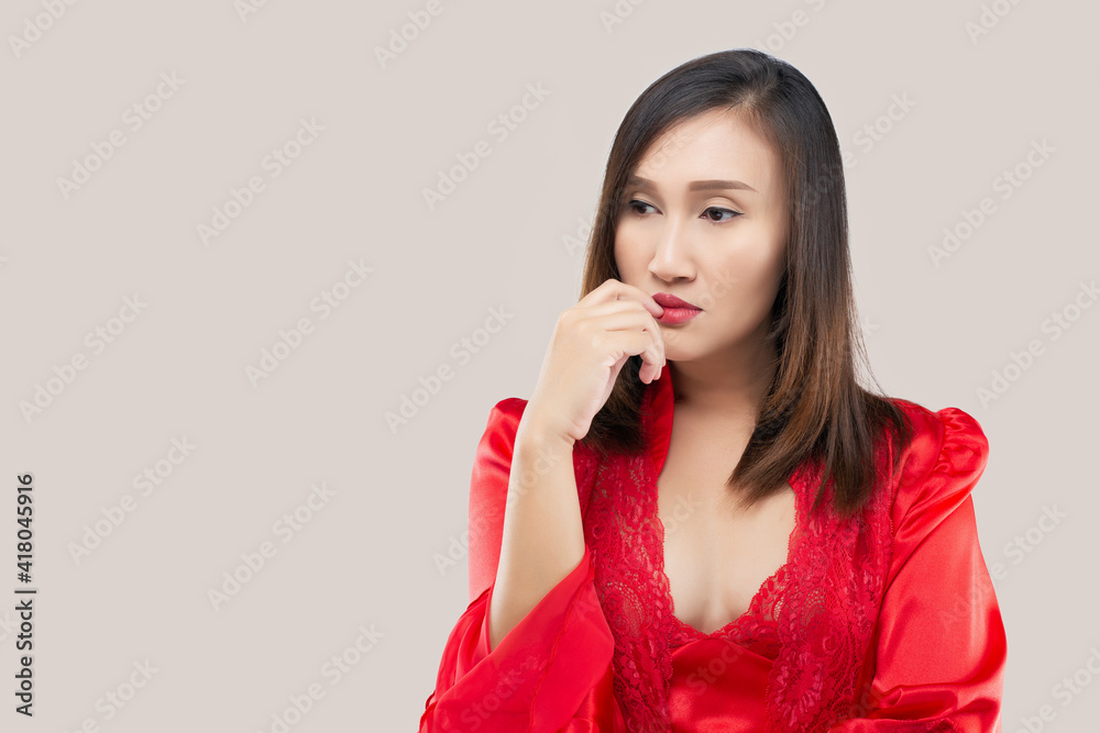 Image of thinking sexy lady standing isolated over pink background. looking away. The hand near the face and mouth. Asian woman in a red satin nightwear wearing lace robe thinking looks left. Image of thinking sexy lady standing isolated over pink background. looking away. The hand near the face and mouth. Asian woman in a red satin nightwear wearing lace robe thinking looks left.