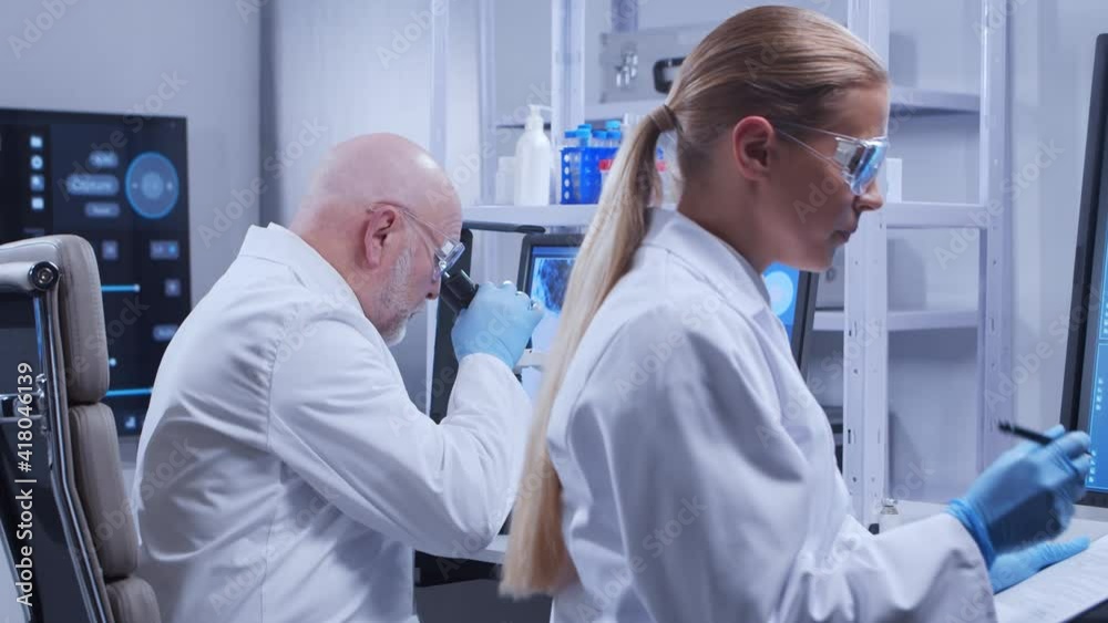 Elderly professor and young laboratory assistant are doing scientific experiment in a modern laboratory. Genetic engineers workplace. The concept of science, medicine and vaccine development. Elderly professor and young laboratory assistant are doing scientific experiment in a modern laboratory. Genetic engineers workplace. The concept of science, medicine and vaccine development.