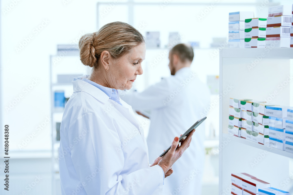 female pharmacist with a digital tablet standing near a shelf with medicines. female pharmacist with a digital tablet standing near a shelf with medicines.