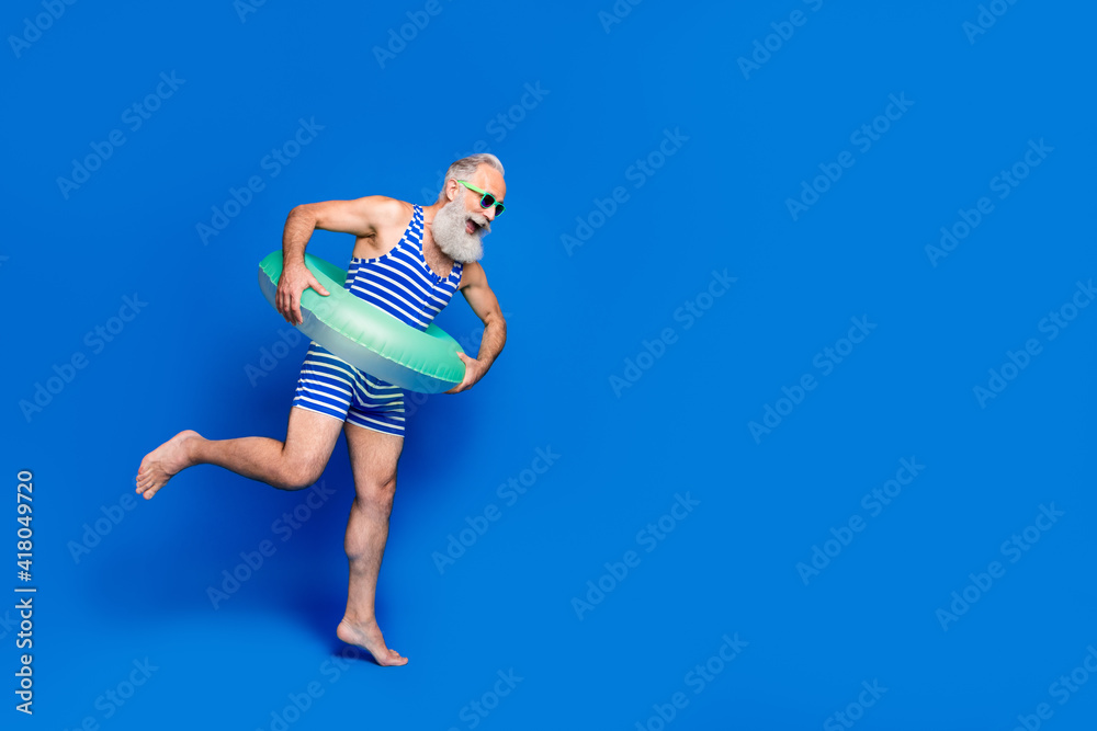 Full size profile side photo of mature smiling man with buoy jumping in pool isolated on blue color background