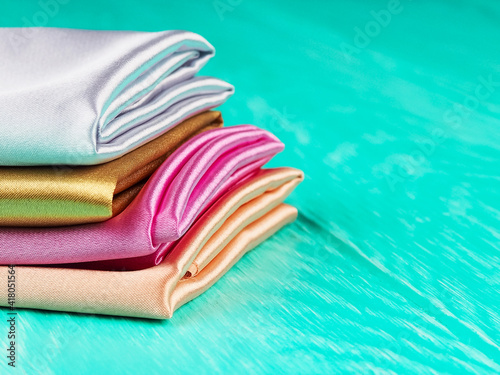 A stack of multi-colored satin fabric on a blue background, space for text
