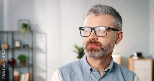Close up portrait of happy joyful handsome middle-aged senior Caucasian man in eyeglasses looking at camera and smiling in good mood at home, positive emotions, cheerful face expression