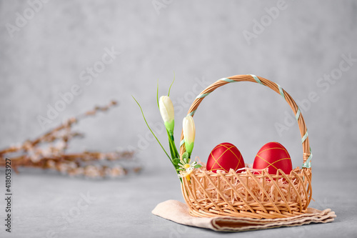 Two red painted Easter eggs in the wicker basket on gray table top with pussy willow branches on backdrop