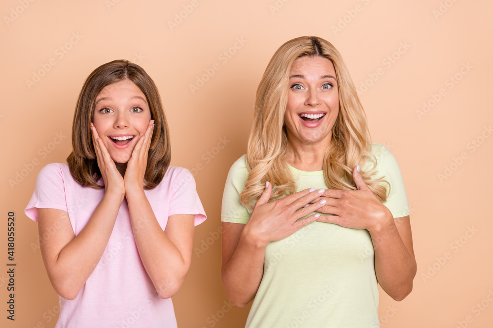 Photo of amazed mother and daughter hold hands chest cheeks news sale isolated on beige color background Photo of amazed mother and daughter hold hands chest cheeks news sale isolated on beige color background