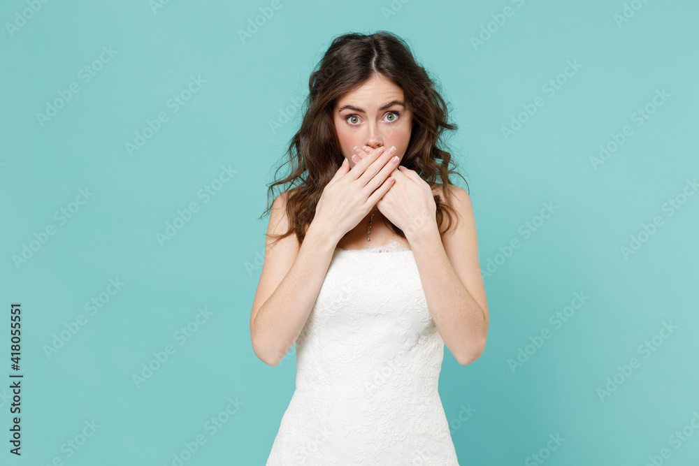 Shocked amazed bride young woman 20s in beautiful white wedding dress covering mouth with hands isolated on blue turquoise color wall background studio portrait. Ceremony celebration party concept.