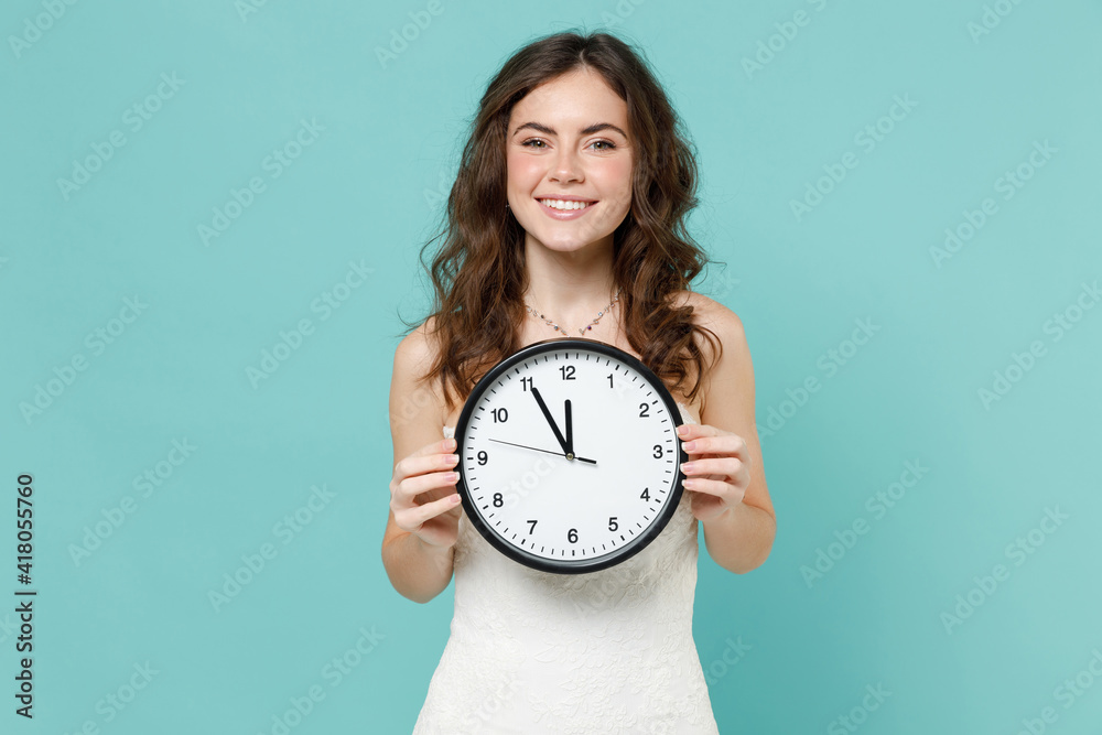 Smiling cheerful bride young woman 20s years old in beautiful white wedding dress hold in hand clock isolated on blue turquoise color background studio portrait. Ceremony celebration party concept. Smiling cheerful bride young woman 20s years old in beautiful white wedding dress hold in hand clock isolated on blue turquoise color background studio portrait. Ceremony celebration party concept.