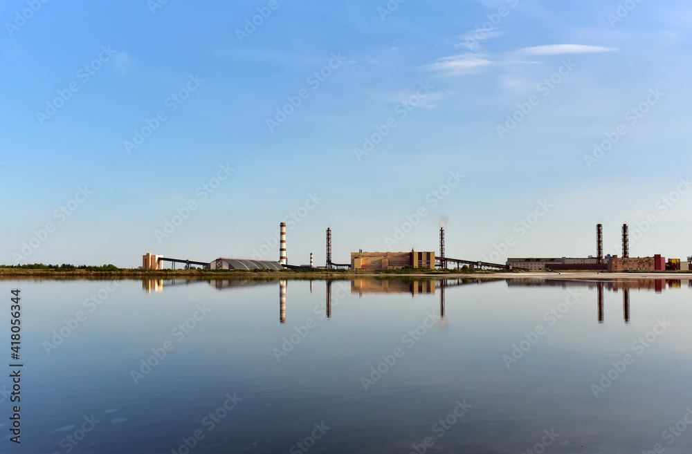 View of an industrial plant with chimneys and workshop buildings near the lake against blue sky. Cleaning Up after pollution. Safe drinking water foundation. Release of toxic substances into the air