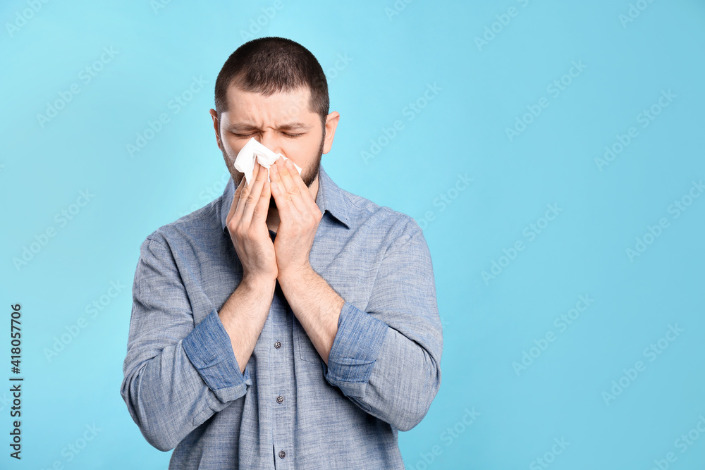 Man with tissue suffering from runny nose on light blue background. Space for text Man with tissue suffering from runny nose on light blue background. Space for text