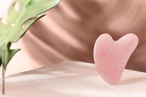 Rose quartz gua sha tool and tropical leaf on table, space for text photo