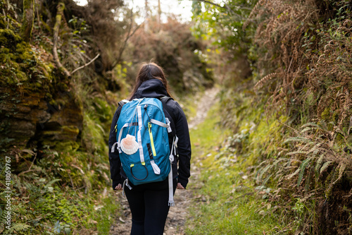 Foto Pilgrim brunette woman, doing the Camino de Santiago, in a forest, with a blue backpack and a shell, with a black jacket