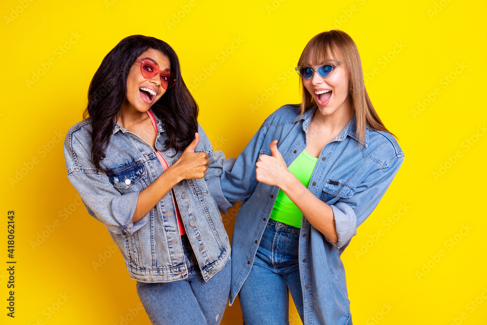 Portrait of two amazed astonished girls open mouth thumb up look camera isolated on yellow color background Portrait of two amazed astonished girls open mouth thumb up look camera isolated on yellow color background