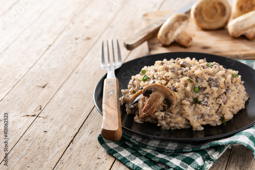 Risotto with mushroom on black plate on wooden table	. Copy space