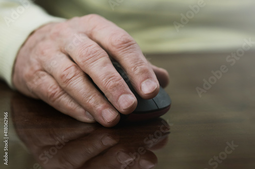 Wrinkled hand of senior man holding computer mouse on table at home.