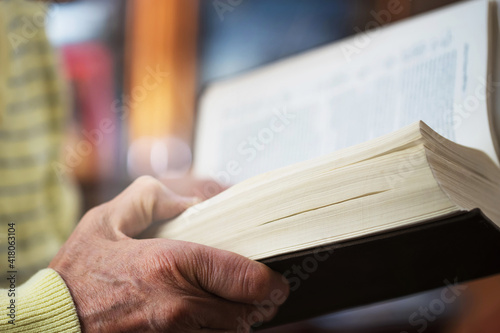 Elderly man holding old Bible book in wrinkled hand and reading pray.