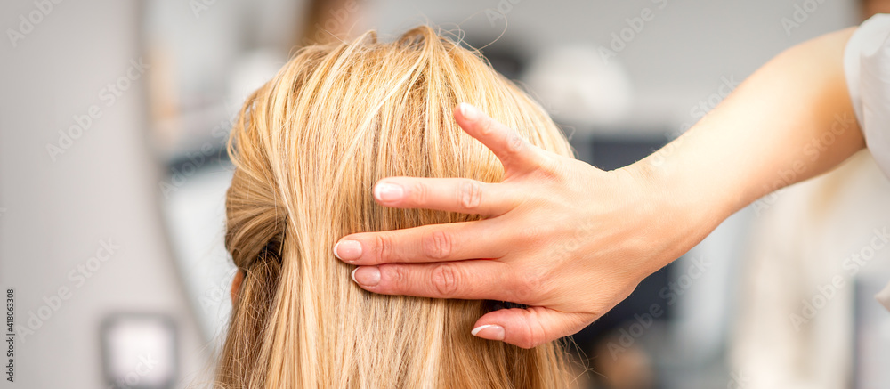 Fototapeta premium Close up of female hairdresser styling blonde hair of a young woman in a beauty salon
