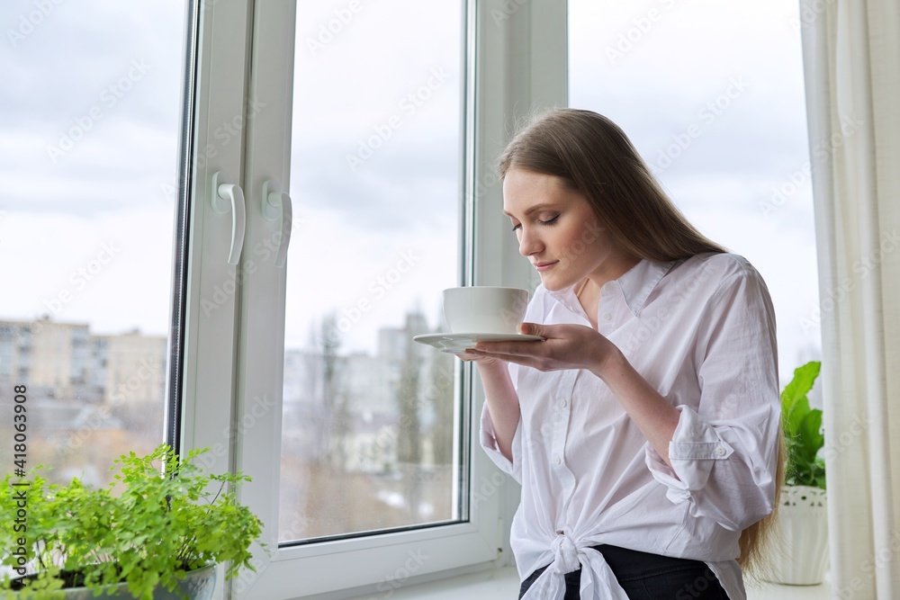 Young beautiful woman with cup of tea at home near window