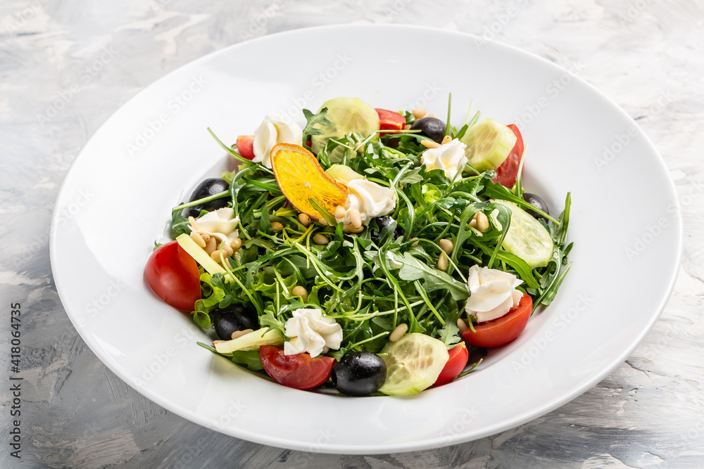 Greek salad of fresh cucumber, tomato, arugula, cream cheese, pine nuts and olives with olive oil. Healthy food, top view