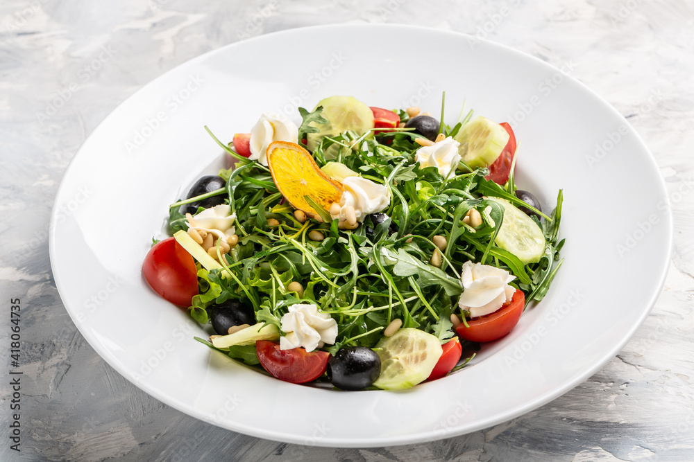 Greek salad of fresh cucumber, tomato, arugula, cream cheese, pine nuts and olives with olive oil. Healthy food, top view Greek salad of fresh cucumber, tomato, arugula, cream cheese, pine nuts and olives with olive oil. Healthy food, top view