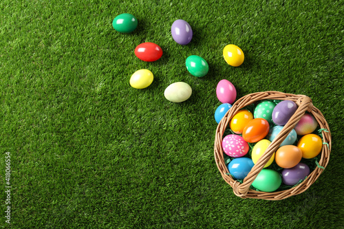 Photography Wicker basket with Easter eggs on green grass, flat lay