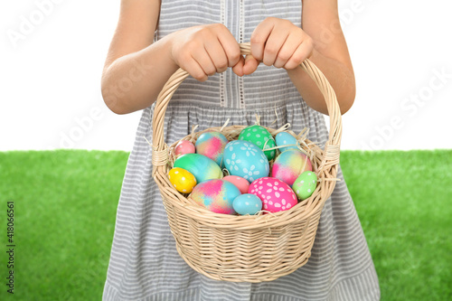 Little girl with basket full of Easter eggs on green grass against white background, closeup