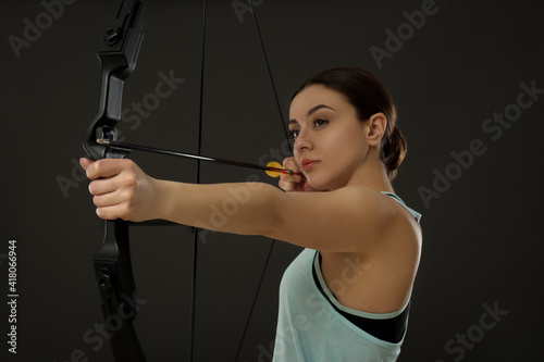Sporty young woman practicing archery on black background