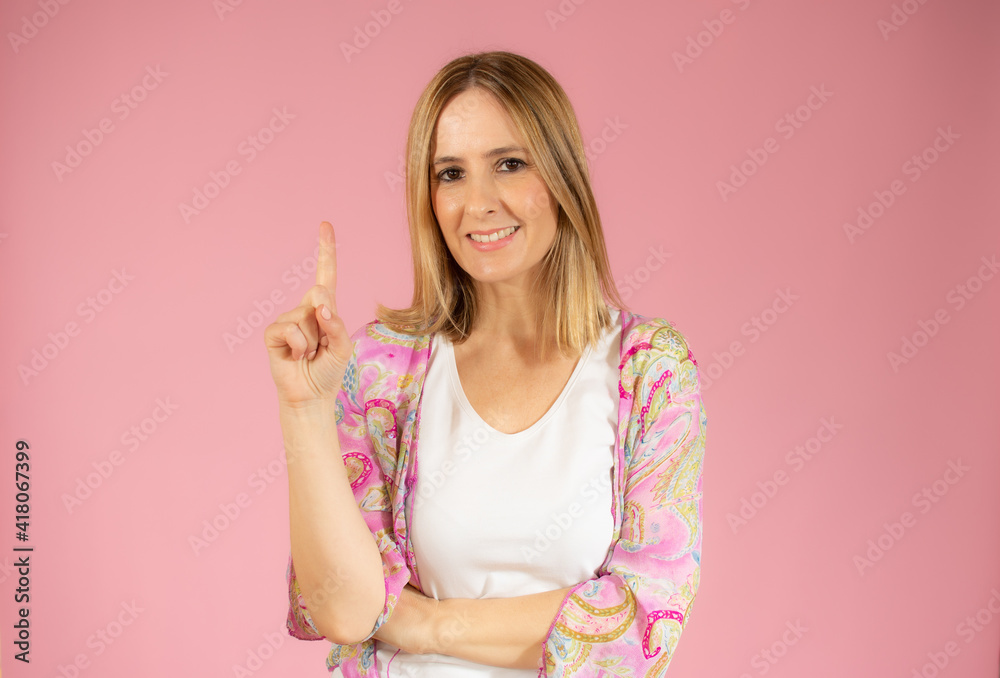 Portrait of beautiful young woman pointing up over pink background.