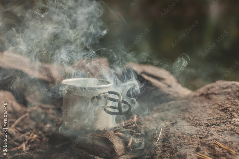 Iron mug on bonfire, in smoke at camping place in forest