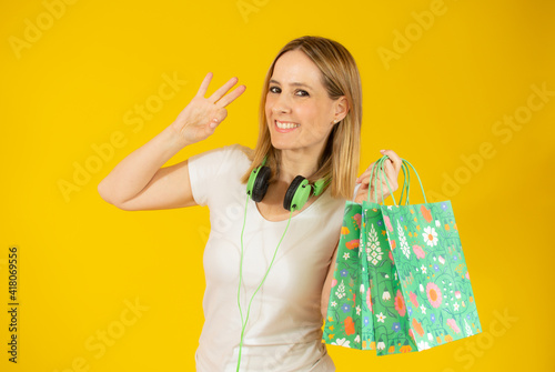 Portrait of a smiling woman holding shopping bags and looking at camera isolated over yellow background