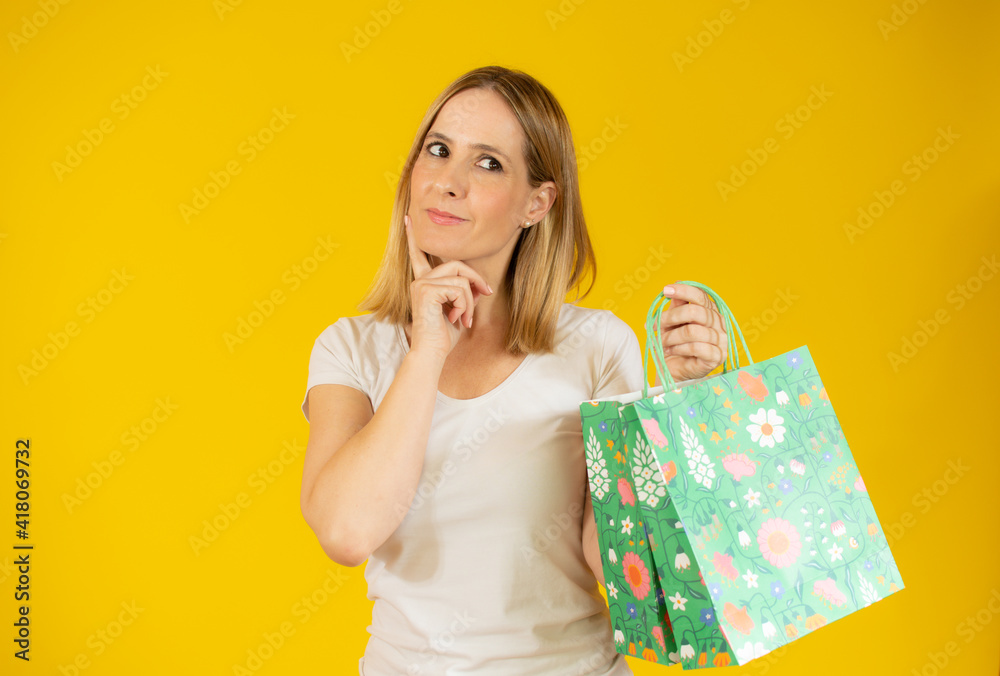 Attractive thoughtful young woman holding shopping bags standing isolated over yellow background Attractive thoughtful young woman holding shopping bags standing isolated over yellow background