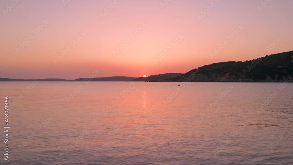 Beautiful seascape at sunset. Sun setting behind a mountain and sea with calm water movement.